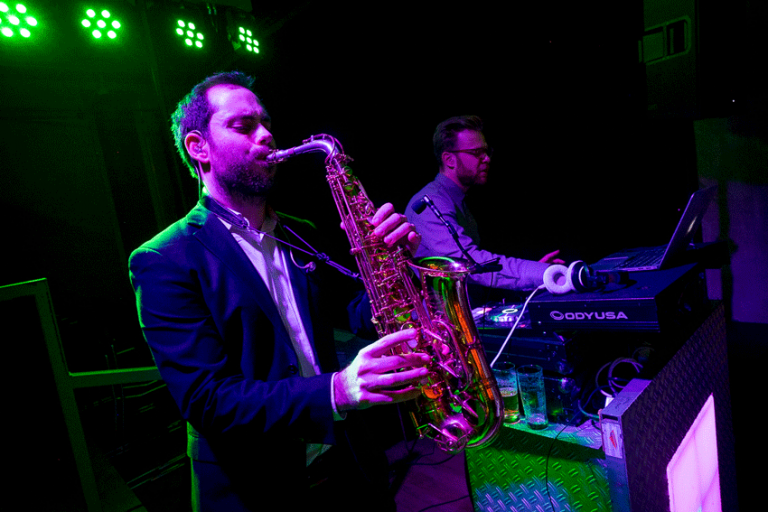 Saxofonist speelt naast de DJ booth met groene feestverlichting
