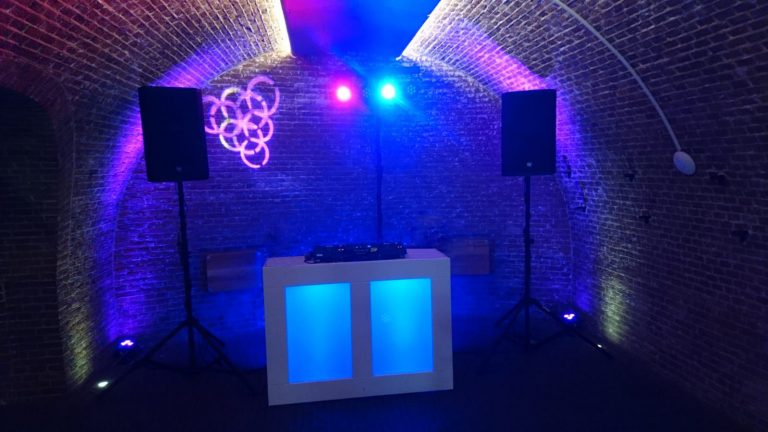 Blauw verlichte DJ booth met speakers voor een bakstenen boog