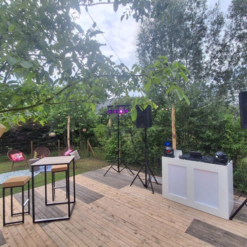 Witte DJ-booth met licht en geluid op een houten terras tijdens een tuinfeest