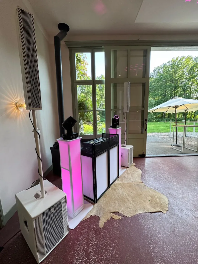 Compacte DJ booth met roze lichtzuilen naast open deuren naar de tuin