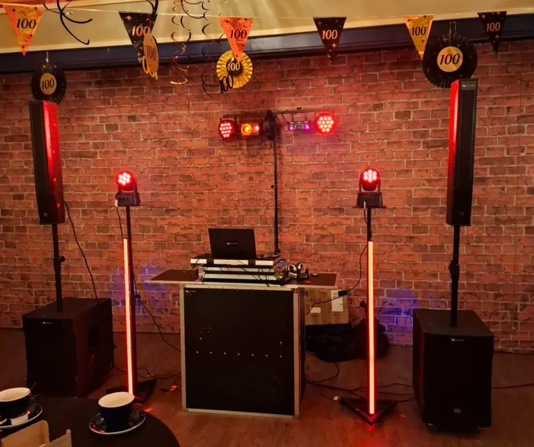 Zwarte DJ booth met twee lichtzuilen en rode feestverlichting voor een bakstenen wand