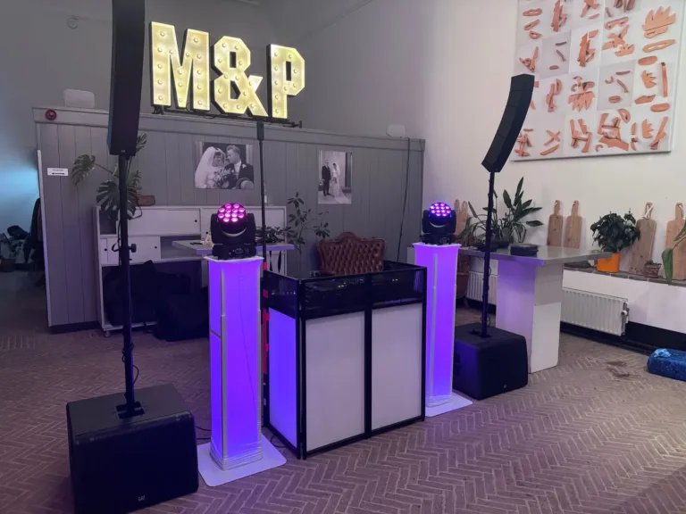 Witte DJ booth met twee paarse lichtzuilen en speakers op een feestlocatie