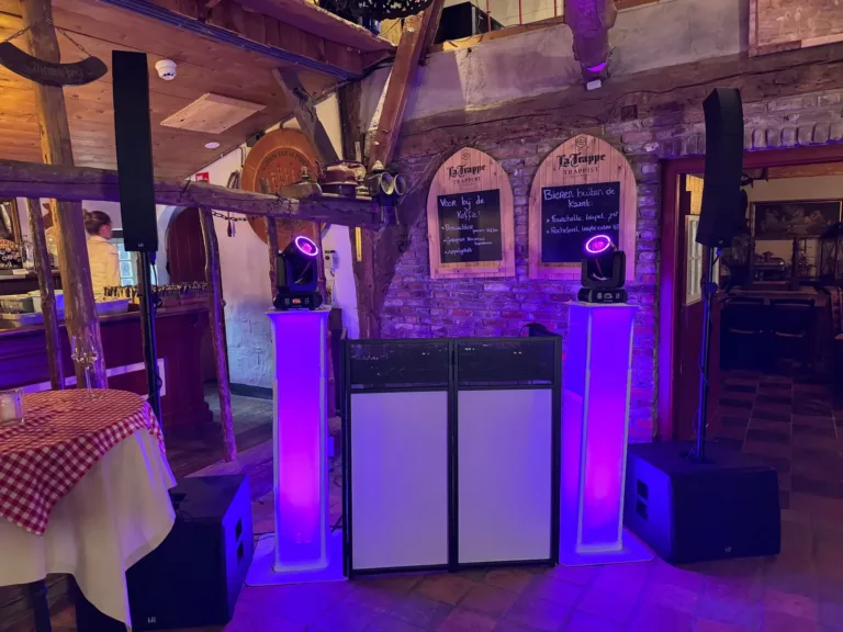 Witte DJ booth met paarse lichtzuilen in een zaal met baksteen en houten balken