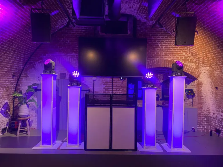 Witte DJ booth en vier paars verlichte lichtzuilen voor een bakstenen wand