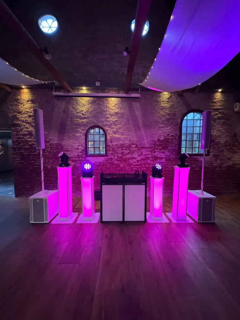 Witte DJ booth met vier roze verlichte lichtzuilen op een houten dansvloer in een kerk