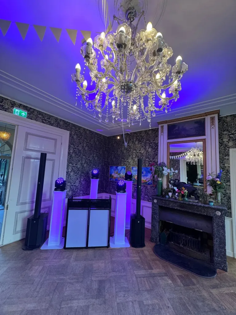 Compacte DJ opstelling met paarse verlichting onder een grote kroonluchter