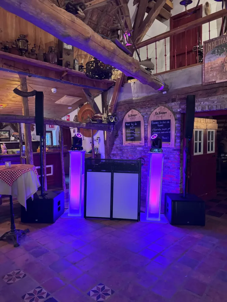 Overzicht van een witte DJ booth en paarse verlichting in een rustieke feestzaal
