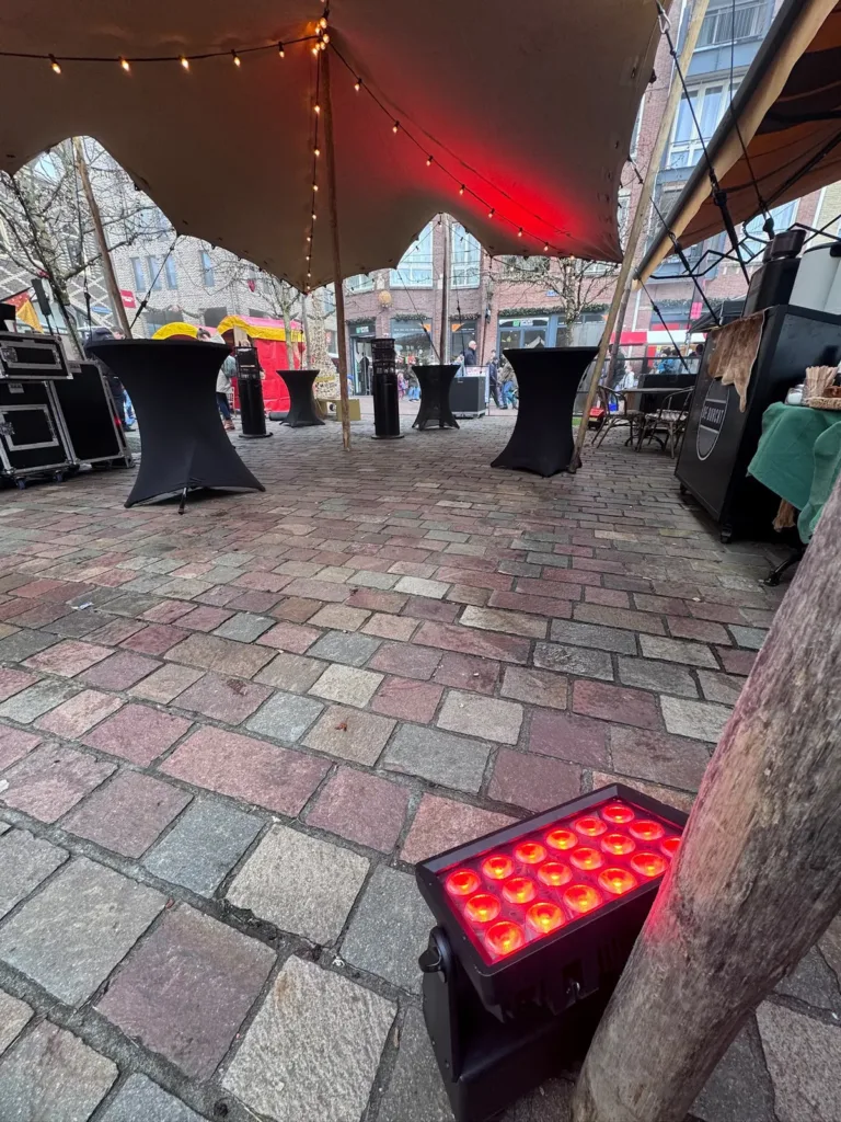 DJ opstelling onder een stretchtent met rode uplighting en statafels