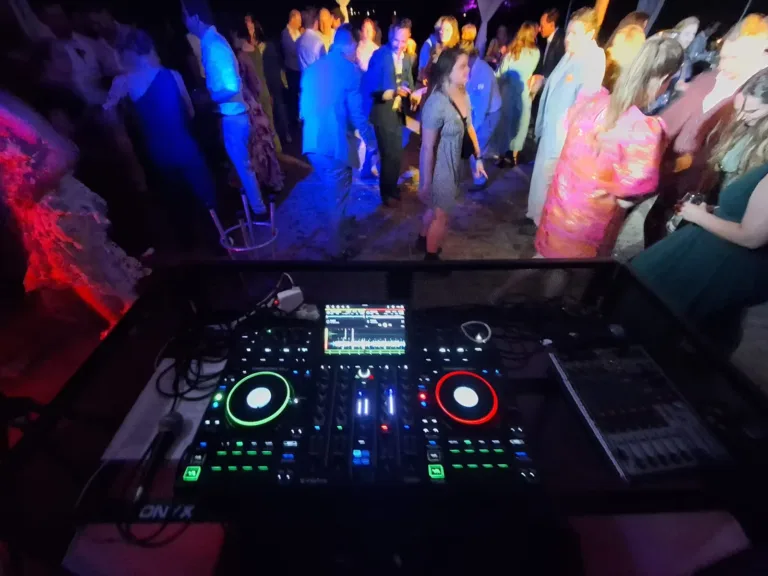 Dansende gasten met blauwe feestverlichting gezien van achter de DJ controller