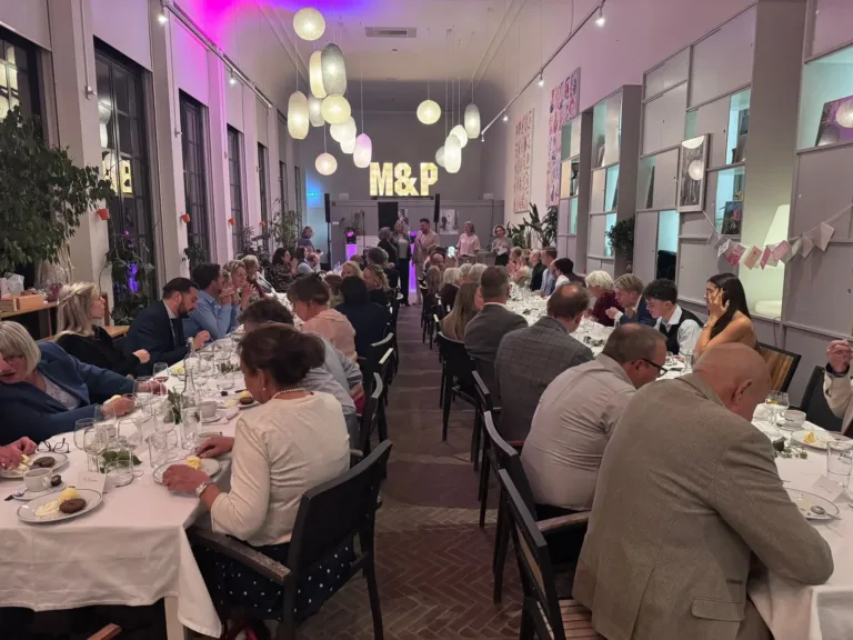 Gasten aan lange gedekte tafels met een DJ opstelling achter in de feestzaal