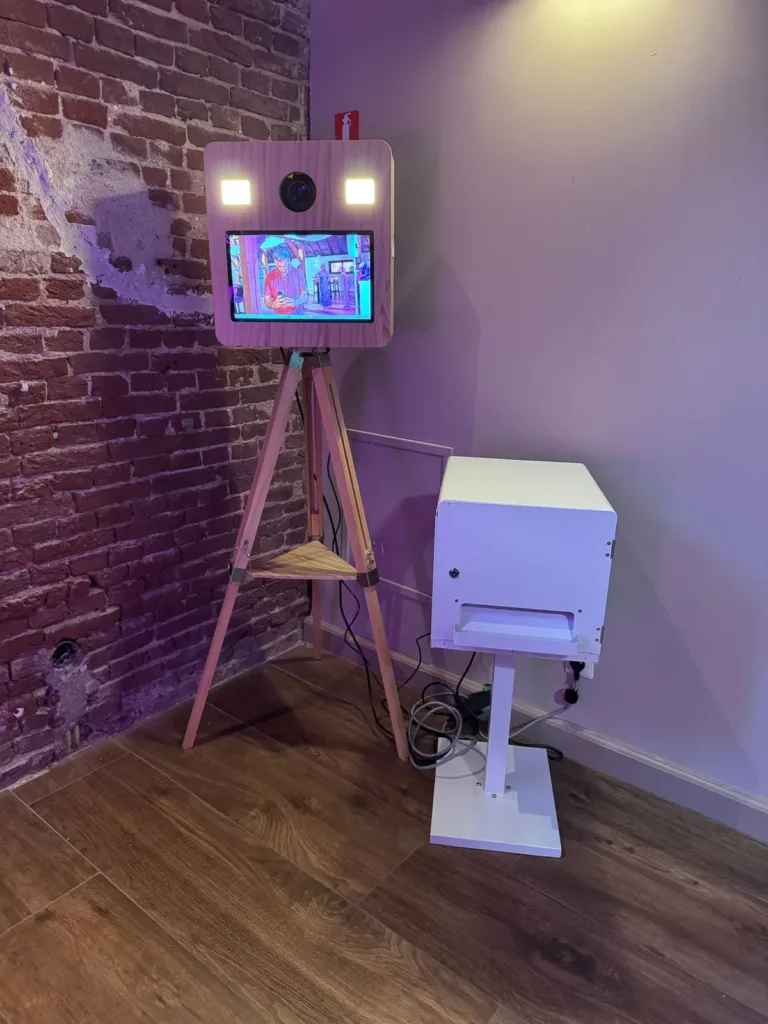 Houten photobooth op statief met een losse fotoprinter naast een bakstenen wand