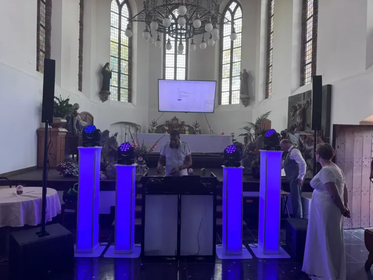 Witte DJ booth met paars verlichte lichtzuilen en speakers in een kerk