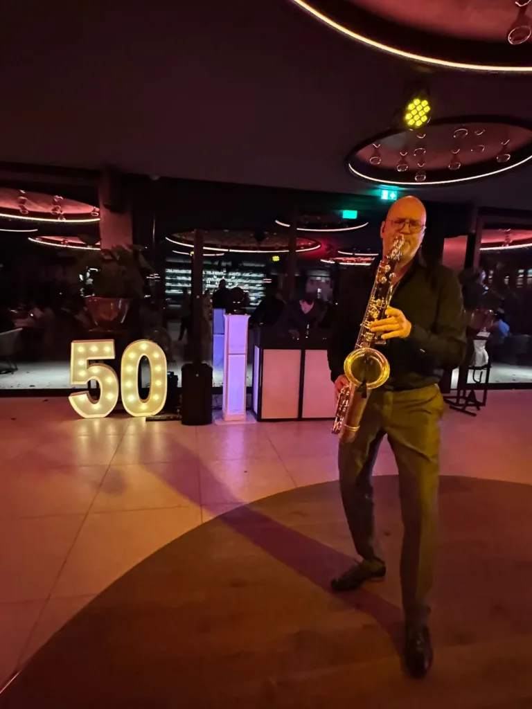Saxofonist speelt op de dansvloer bij een verlicht cijfer 50 en een DJ booth