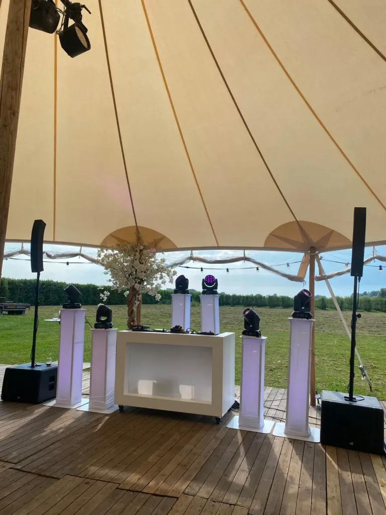 Witte DJ booth met vier lichtzuilen onder een stretchtent met uitzicht op het weiland