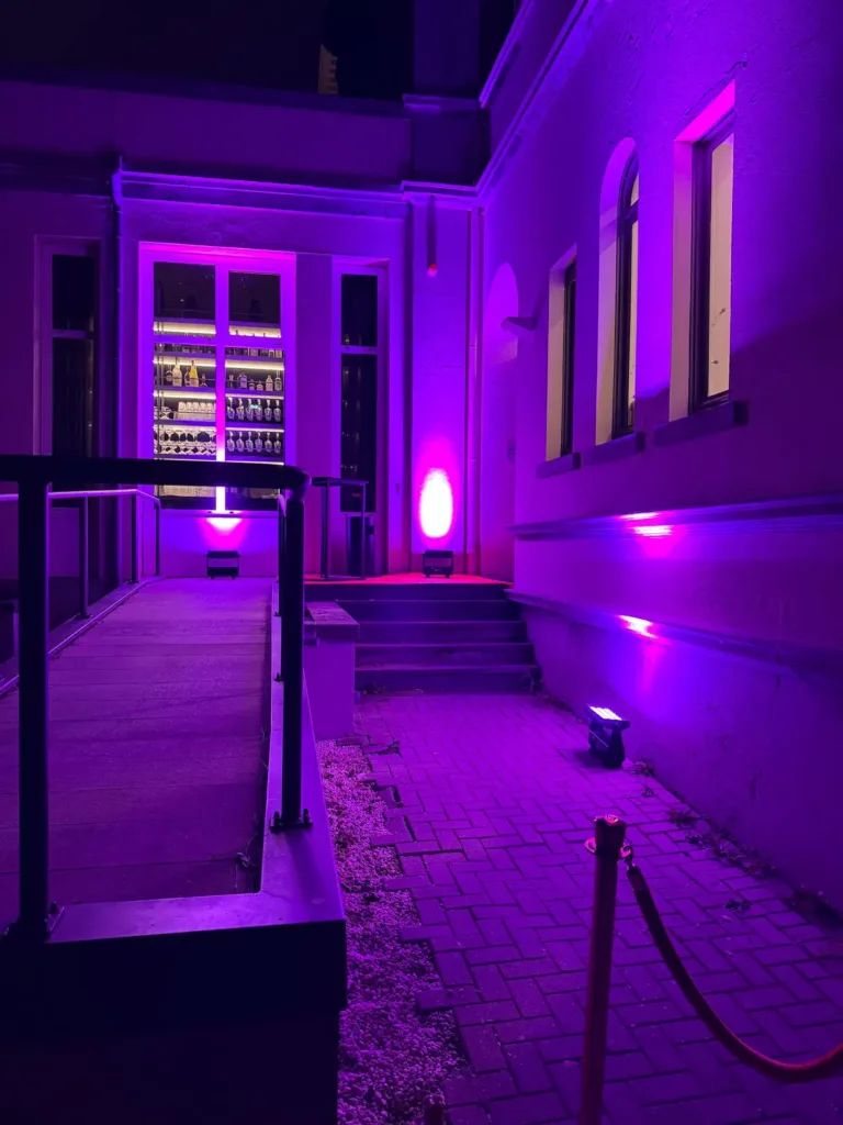 Paarse uplighting verlicht de muren en hoge ramen naast de dansvloer