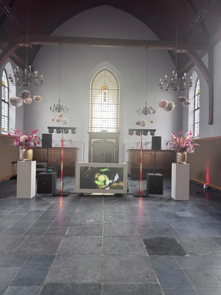 Symmetrische witte DJ opstelling met speakers en lichtzuilen in een kerk met hoge ramen